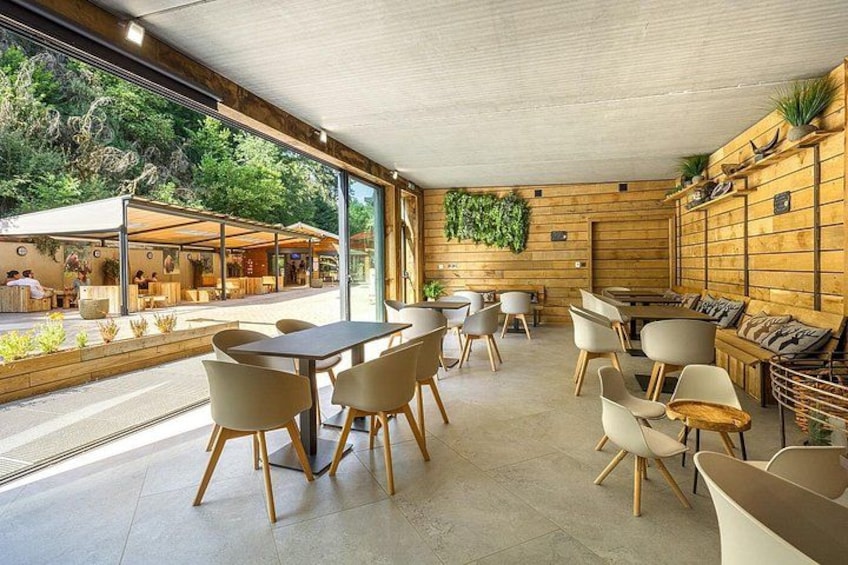 An indoor cafe with wooden walls, a large window, and a seating area with tables and chairs. 2