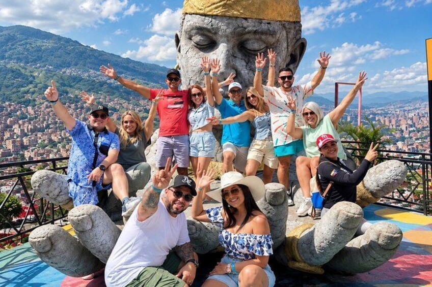A group of people posing with a large stone sculpture of a face, with a cityscape in the background. 1