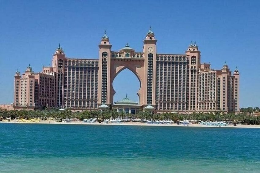 A large hotel with a distinctive arch entrance, a beach in the foreground, and clear blue water. 5