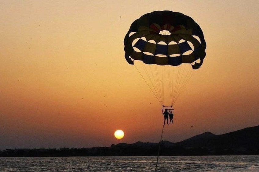 Un atardecer con un paracaídas y dos personas descendiendo sobre una masa de agua. 2