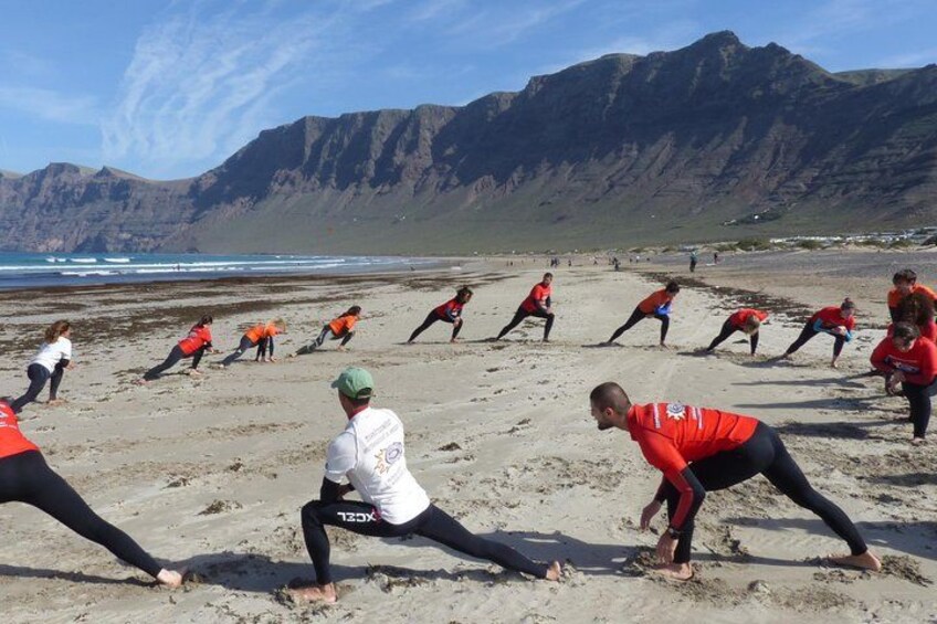 Un groupe de personnes fait des étirements sur une plage, avec des montagnes en arrière-plan. 3
