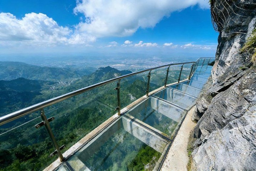 A glass walkway with metal railings overlooking a mountainous landscape. 4