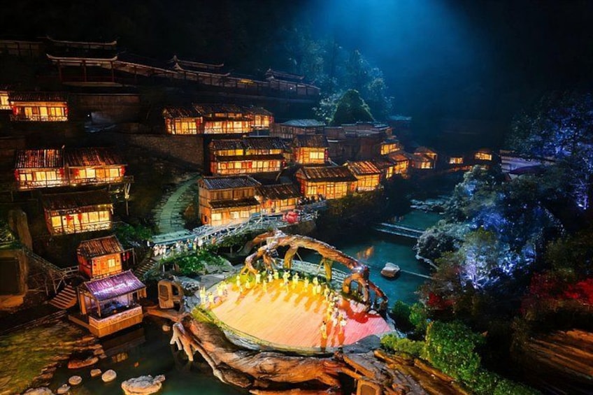 A traditional village at night with illuminated buildings and a central water feature. 5