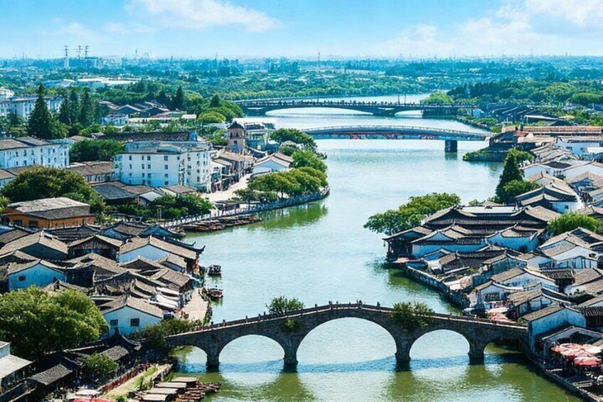 A river with traditional buildings on both sides, a stone bridge, and a distant cityscape. 3