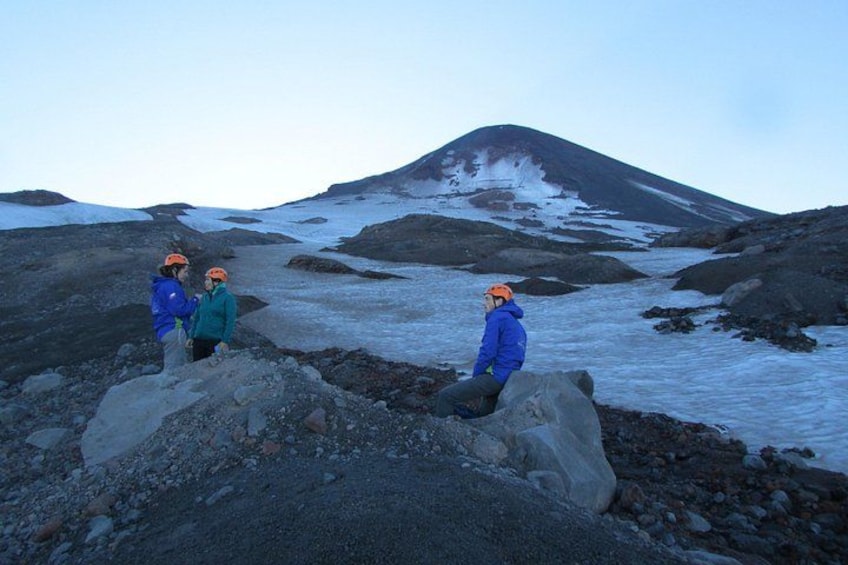 Un grupo de personas con equipo de senderismo en un terreno rocoso, con un glaciar y una montaña al fondo. 3