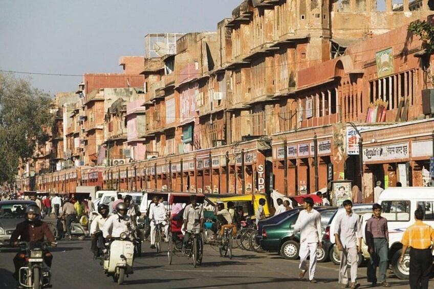 A busy street with motorcycles, bicycles, and pedestrians. There are multi-story buildings with shops on the ground floor. 3