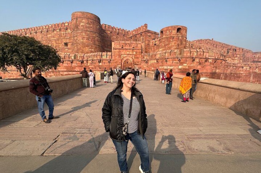A historic fort with red walls and a large central tower, surrounded by a paved walkway with people walking. 3