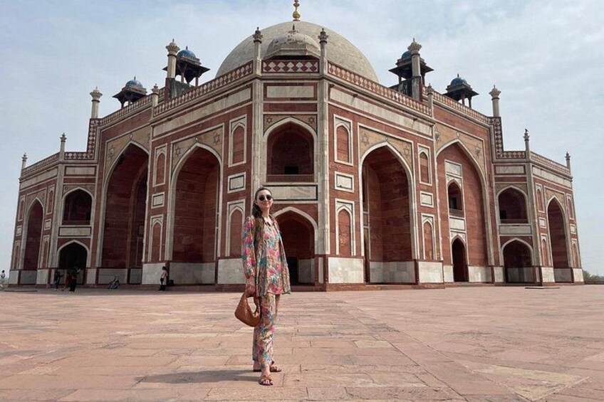 A large, historic building with domes and arches, a paved plaza, and a person standing in the foreground. 2