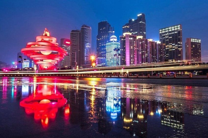 A city skyline with illuminated buildings and a distinctive red structure reflecting on the water. 1