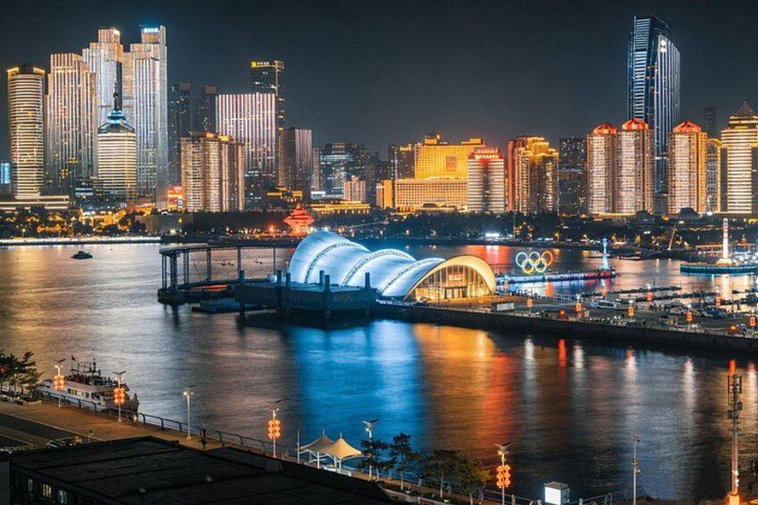 A city skyline at night with illuminated buildings, a river, and a stadium with the Olympic rings. 2