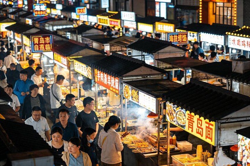A bustling night market with food stalls and people shopping. 5