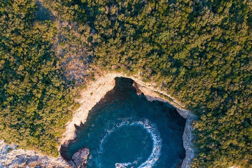 Vue aérienne d’une zone côtière avec une formation rocheuse circulaire entourée d’une forêt dense. 2