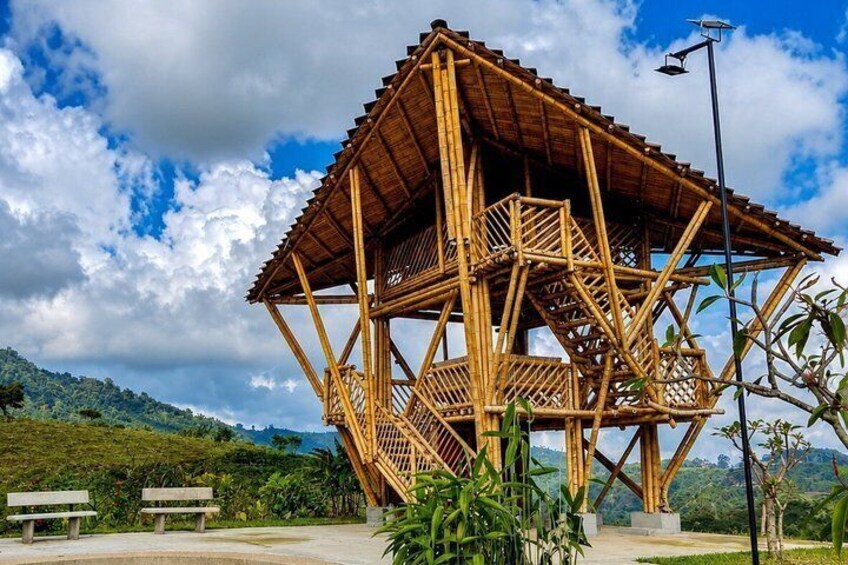 A wooden gazebo with a hexagonal shape, surrounded by lush greenery and a clear sky. 3