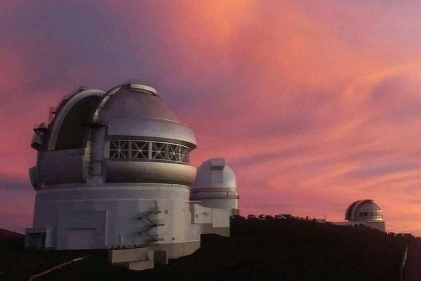 Una grande cupola di un osservatorio con una cupola più piccola sullo sfondo, su uno sfondo di cielo al tramonto. 1