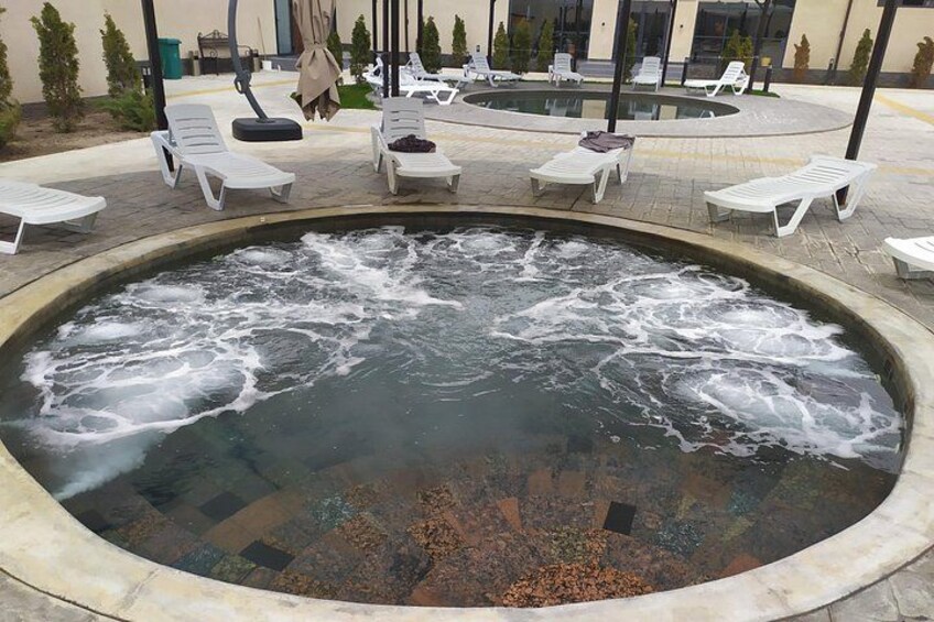 A hot spring with water flowing, surrounded by lounge chairs and a pool area. 4