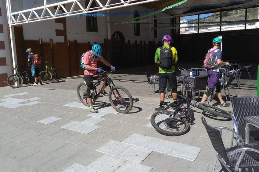 A group of cyclists at a paved outdoor area with bicycles and a building in the background. 1