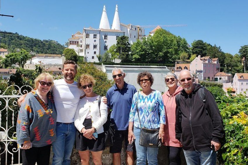 Un grupo de personas frente a un edificio blanco con dos torres, rodeado de vegetación y otros edificios. 3