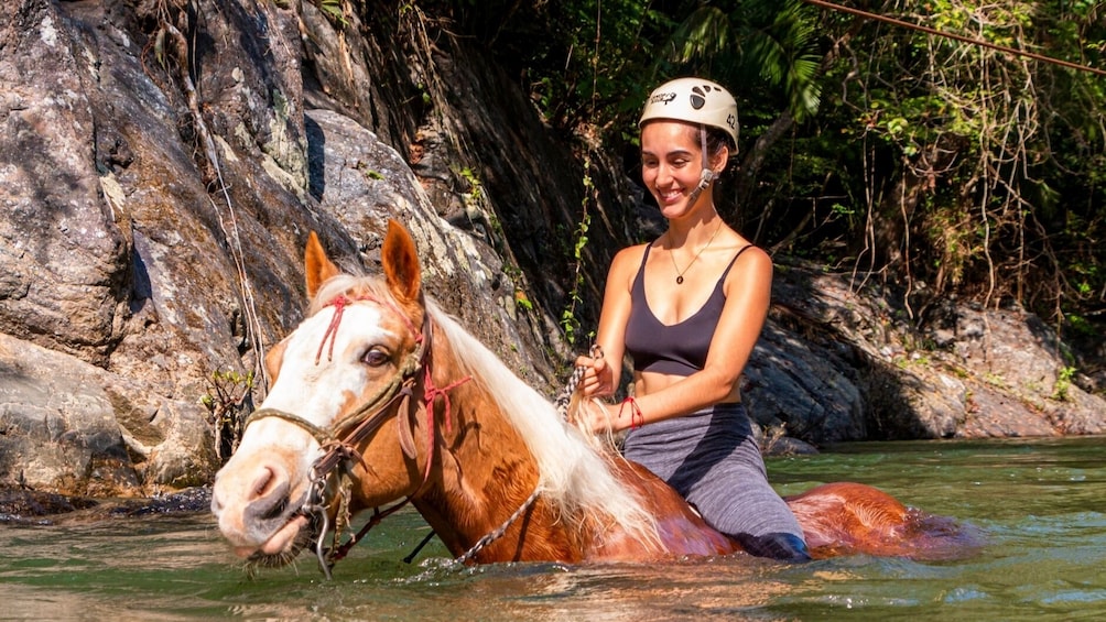 Woman wades through deep river on horseback