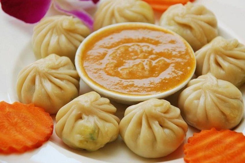 A plate of dumplings with a dipping sauce and carrot slices. 4