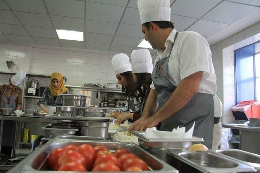 Chefs preparing food in a commercial kitchen with stainless steel equipment and ingredients like tomatoes. 2