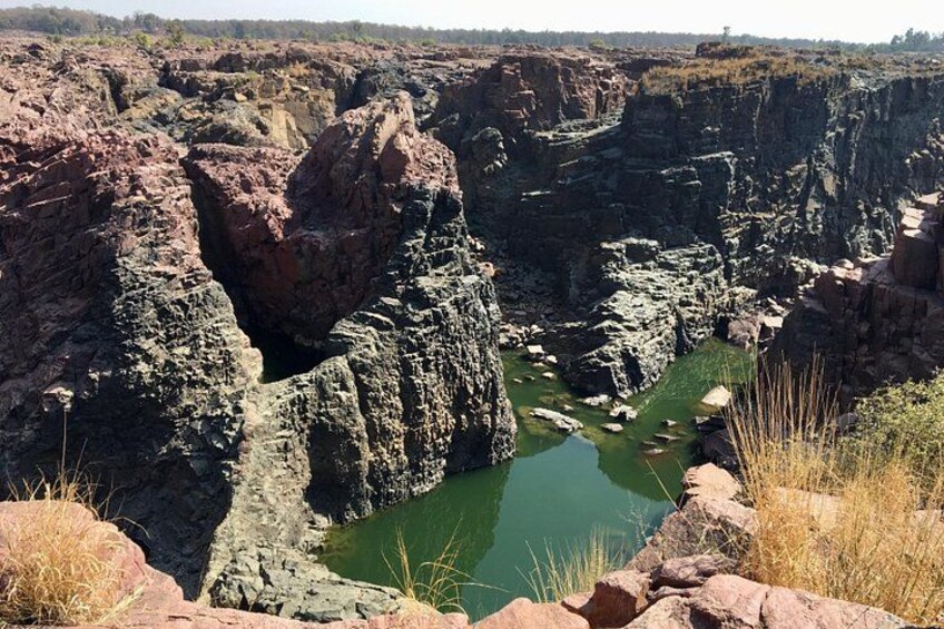 A canyon with a green pool surrounded by rocky cliffs. 1
