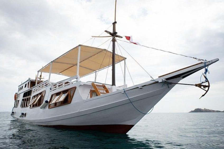 Eine weiße Segelyacht mit Sonnensegel und einer roten Flagge am Mast, die auf ruhigem Wasser treibt. 4