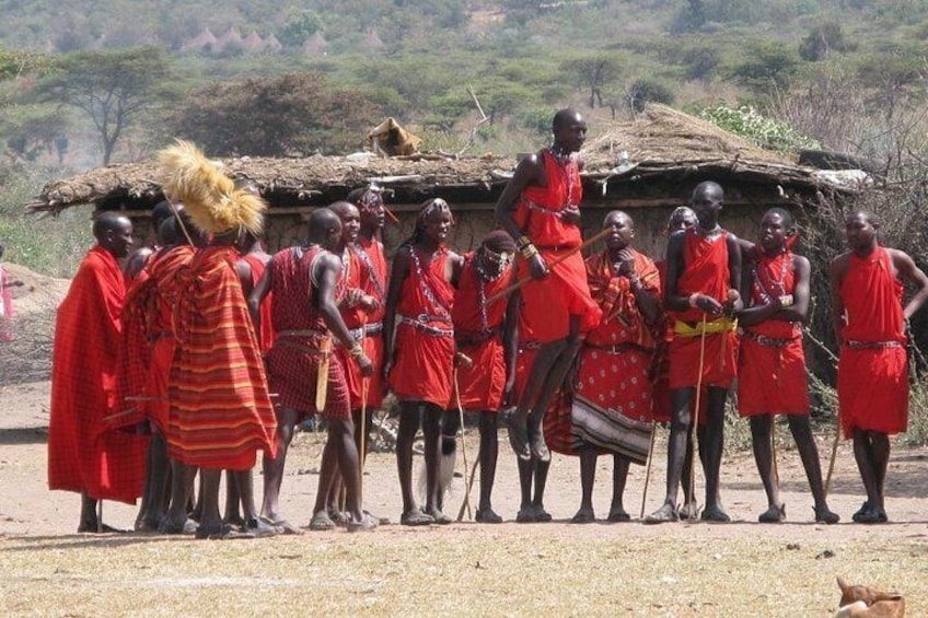 Un grupo de personas vestidas con atuendos rojos tradicionales de pie en fila, con una estructura de techo de paja al fondo. 5