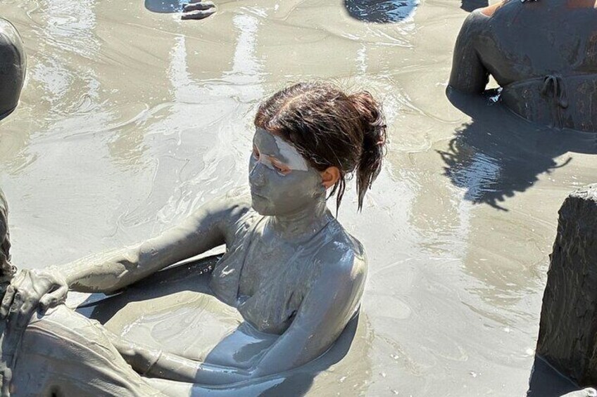 A person sitting in a muddy water body, surrounded by others engaged in similar activities. 2