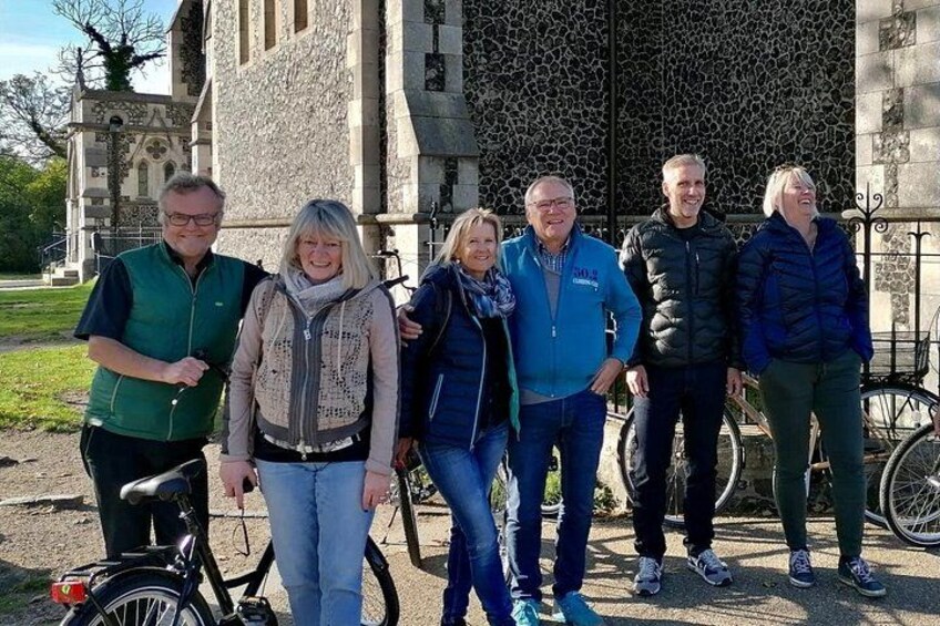A group of people standing in front of a stone building with a large window and a bicycle. 2