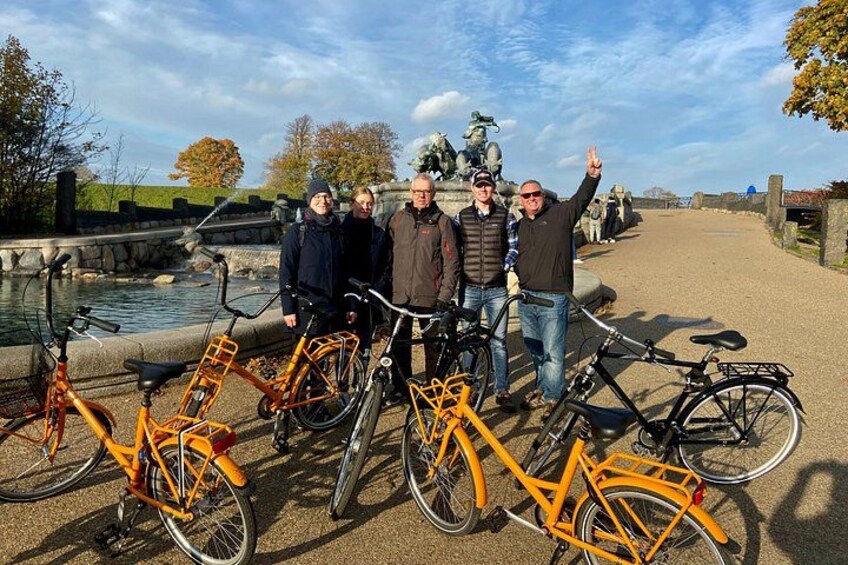 A group of people standing by bicycles near a canal with a statue in the background. 3