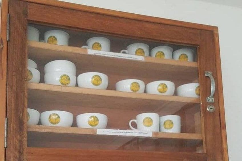 Un mobile in legno con ante in vetro che contiene tazze bianche con decorazioni gialle. 2