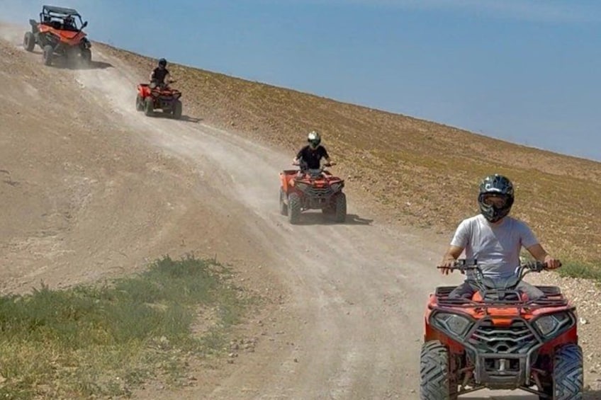 Three off-road vehicles on a dirt path with a hilly landscape in the background. 2