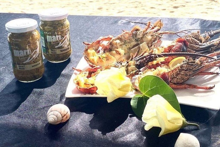 A lobster meal on a plate with lemon slices, a snail, and two jars of sauce. 2