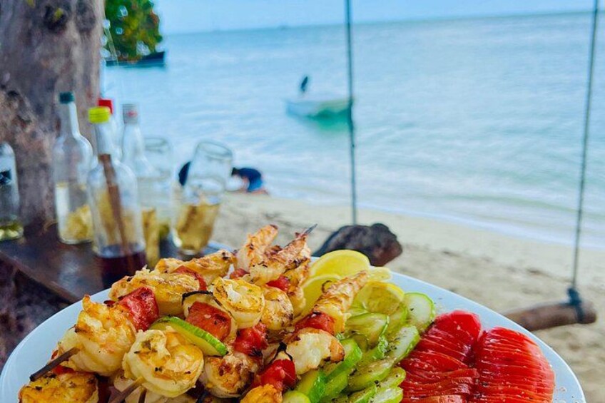 Un plato de camarones a la parrilla y verduras en una playa con el océano al fondo. 5