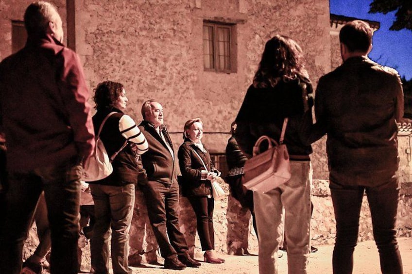 A group of people standing in front of a stone building with a window. 4