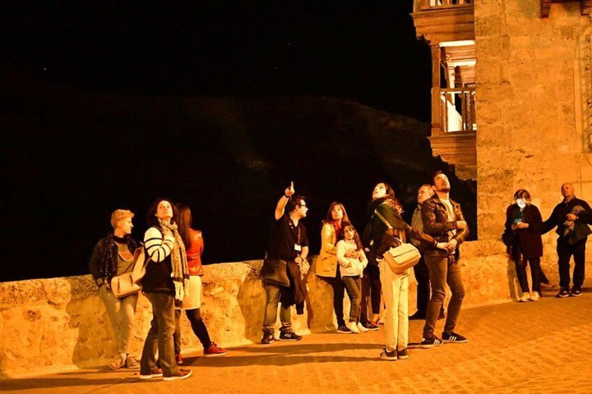 A group of people standing on a paved area at night, with a building in the background. 2