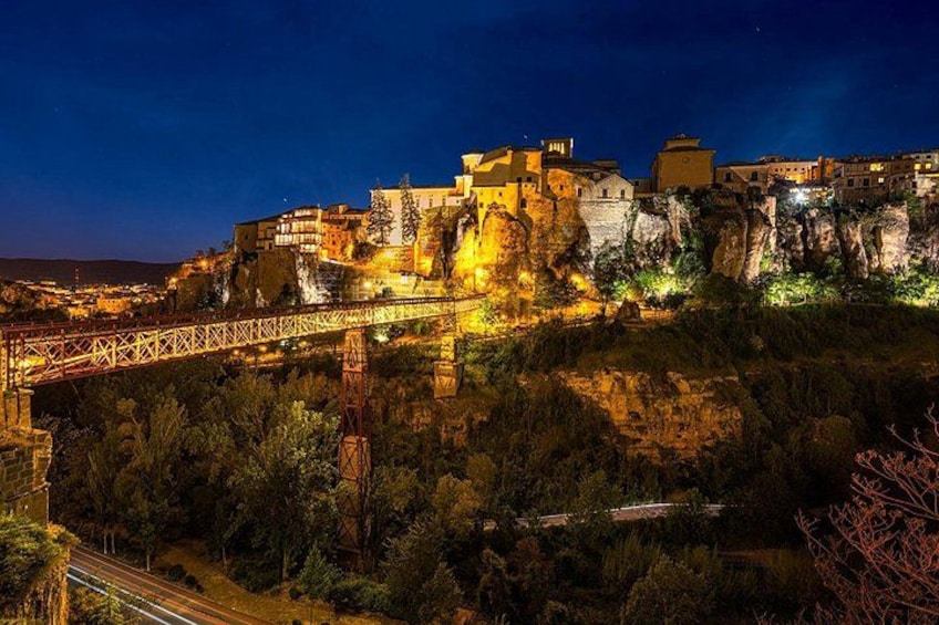 A historic town with a prominent castle on a cliff, a bridge, and surrounding greenery. 1