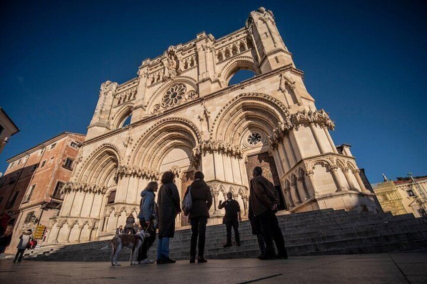A historic cathedral with intricate architecture, a group of people standing in front, and a clear blue sky. 5