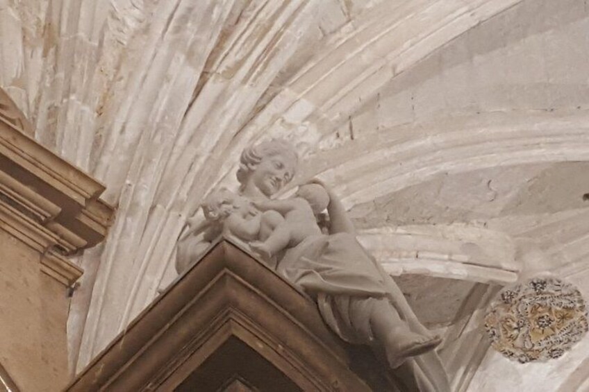 A stone carving of a cherub holding a child on a ceiling. 4