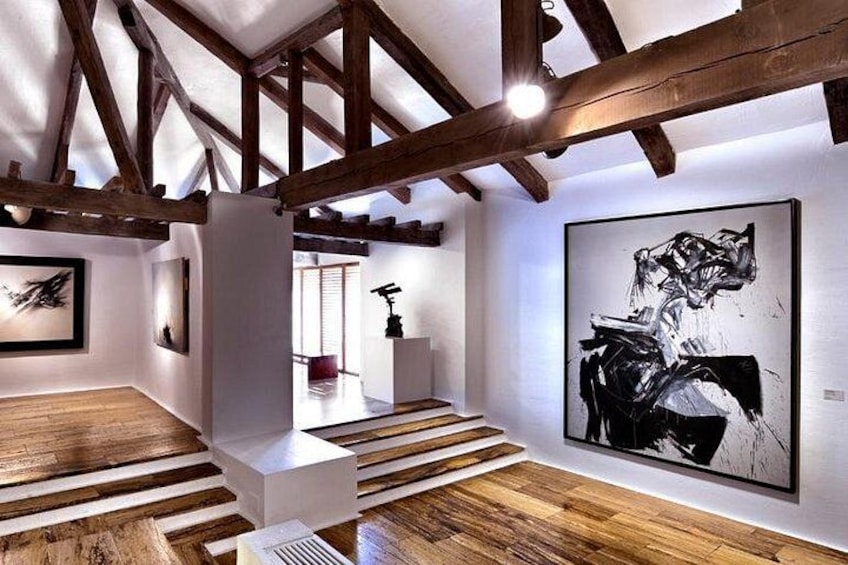 Een kunstgalerie met houten balken, een trap en abstracte schilderijen. 4