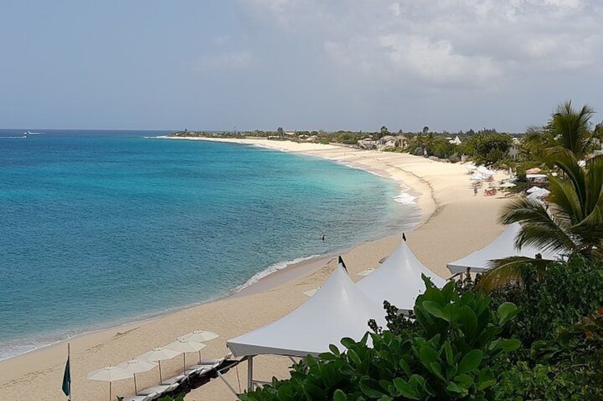 A beach with white tents, clear turquoise water, and a distant shoreline. 2
