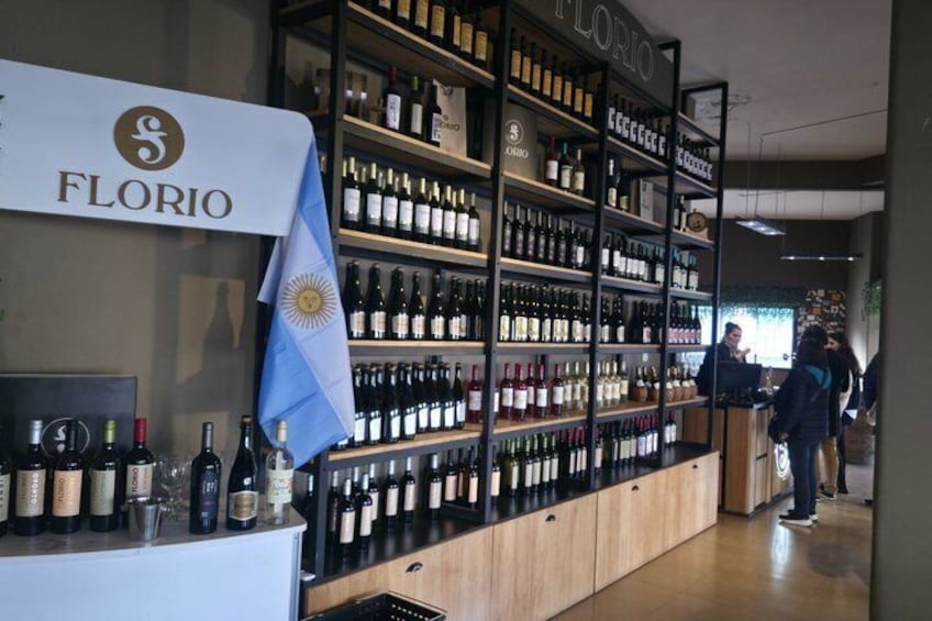 A wine shop interior with shelves of wine bottles, a counter with a name sign, and a flag. 2