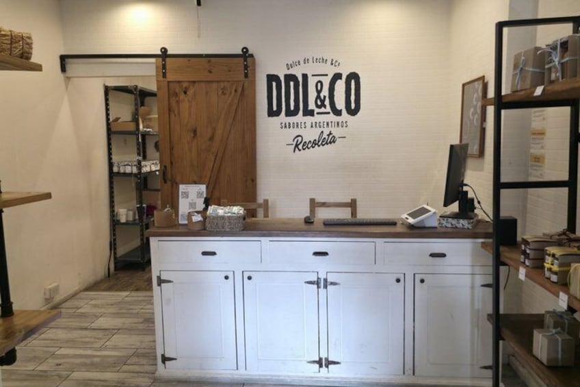 A store interior with a counter, white cabinets, a wooden door, and shelves with products. 5