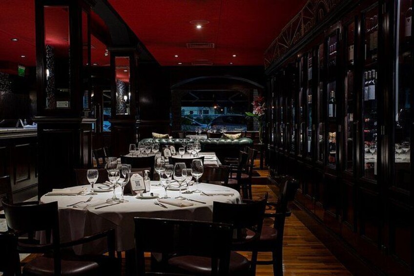 A dimly lit restaurant with tables set for dining, a bar area, and a view of the cityscape through large windows. 2