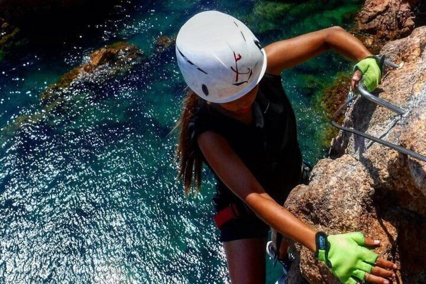 A person rappelling down a rocky cliff with a helmet and gloves, near a body of water. 5