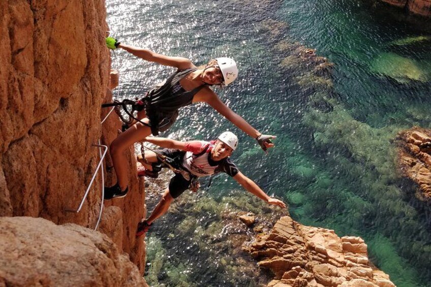 Two people rappelling down a cliff with clear water below. 3