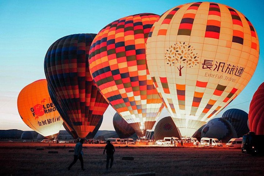 Multiple hot air balloons in a field with people walking around. 2
