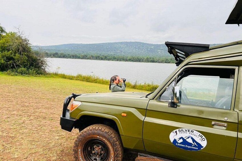 A green off-road vehicle parked by a lake with a person taking a photo. 2
