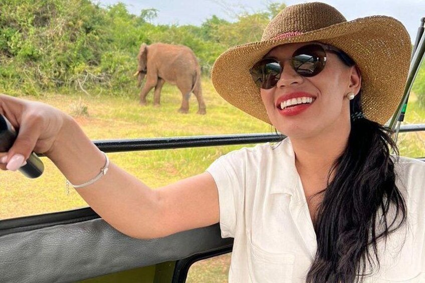 A person in a safari vehicle with a straw hat, holding a camera, and an elephant in the background. 4