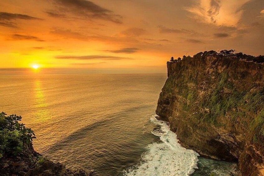 A sunset over a coastal cliff with waves crashing below. 2